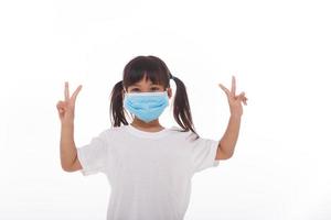 liten asiatisk flicka bär mask innehav händer upp med två fingrar foto