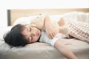barn liten flicka sover i de säng med en leksak teddy Björn foto