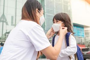 asiatisk mor hjälper henne dotter bär en medicinsk mask för skydd covid-19 eller coronavirus utbrott förbereda till gå till skola när tillbaka till skola ordning. foto