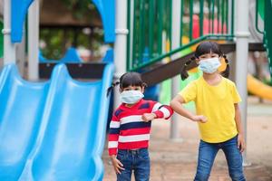 ny vanligt livsstil, social avstånds begrepp. Lycklig barn bär ansikte mask har roligt på på lekplats skydda coronavirus covid19, foto