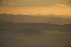 lager av bergen och dimma under solnedgång foto