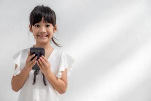 Foto av en liten flicka använder sig av en mobil telefon isolerat över vit bakgrund