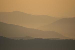 lager av bergen och dimma under solnedgång foto