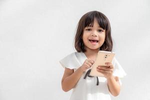 upphetsad asiatisk liten flicka är använder sig av en smartphone, tömma Plats skott isolerat på vit bakgrund foto