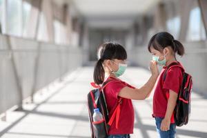 liten flicka och syster bär ansikte mask gående till skola under coronavirus utbrott. säkerhet mask för sjukdom förebyggande. mamma och unge på skola under covid 19 pandemier. foto
