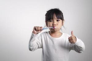 liten söt bebis flicka rengöring henne tänder med tandborste på vit bakgrund foto