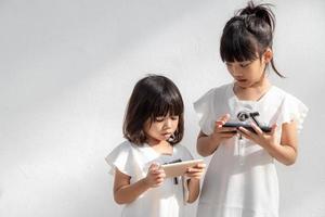 begrepp barn och prylar. två liten flickor syskon systrar se på de telefon. de håll en smartphone Kolla på videoklipp, lära sig, spela spel, tala uppkopplad. internet för barn. foto