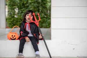 asiatisk barn flicka i demon kostym innehav svart och röd treudd, Lycklig halloween begrepp foto