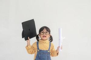 asiatisk liten flicka bär en gradering keps och innehav diplom på vit bakgrund foto