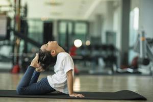 liten söt flicka praktiserande yoga utgör på en matta inomhus- foto