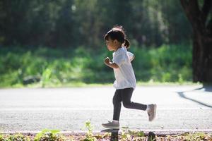 Lycklig barn flicka löpning i de parkera i sommar i natur. värma solljus blossa. asiatisk liten är löpning i en parkera. utomhus- sporter och kondition, övning och konkurrens inlärning för unge utveckling. foto