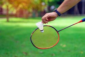 en person innehav en fjäderboll i främre av en badminton racket, begrepp för utomhus- badminton spelar i fri gånger, mjuk och selektiv fokus. foto