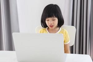 liten asiatisk flicka studerande studie uppkopplad använder sig av bärbar dator dator på Hem foto