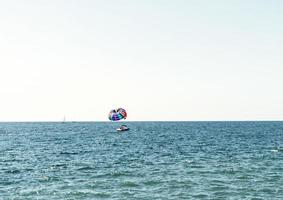 parasailing flerfärgad regnbåge fallskärm Bakom båt över blå turkos hav landskap sommar aktiviteter kopia Plats selektiv fokus foto