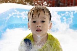 söt liten asiatisk pojke simning i bubblor i ett uppblåsbar slå samman. sommar vatten spela, familj lycka, barns lycka, slå samman och flerfärgad bollar foto