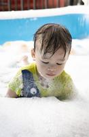 liten asiatisk pojke åtnjuter simning och spelar med bubblor i ett uppblåsbar slå samman. sommar vatten spela, familj lycka, barns lycka. vertikal bild foto
