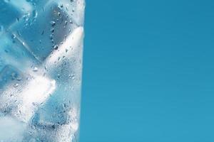 en glas med is vatten och is kuber på en blå bakgrund. foto