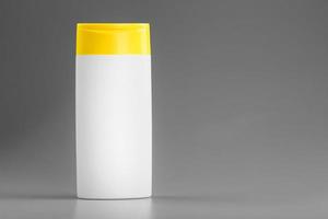 vit flaska av schampo och dusch gel med gul keps på grå bakgrund foto
