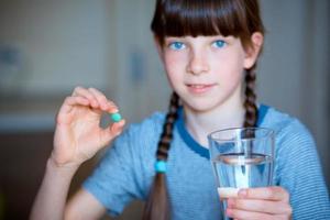 kapslar, piller i ett hand, en glas av vatten i de Övrig. de flicka är innehav de medicin i främre av henne. närbild. foto