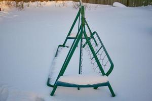 snötäckt trädgård gunga. trä- trädgård gunga på kedjor, Allt i de snö. gunga i vinter. foto