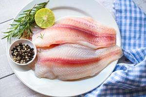 kött dolly fisk tilapia randig havskatt, färsk rå pangasius fisk filea med ört och kryddor citron- kalk och rosmarin, fisk filea på vit tallrik med Ingredienser för matlagning foto