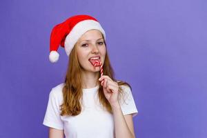en glad flicka i santa hatt är äter klubba och skrattande i vit t-shirt. foto