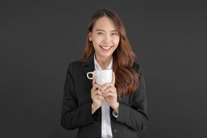 företag kvinna bär en svart kostym stående med en kopp av kaffe. foto