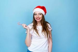 Söt kvinna i santa hatt innehav röd och vit jul klubba i vit foto
