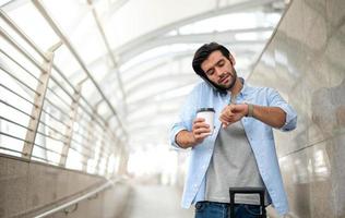 de man använder sig av de smartphone och ser de hand Kolla på medan han skynda till kolla upp i på de flygplats. foto