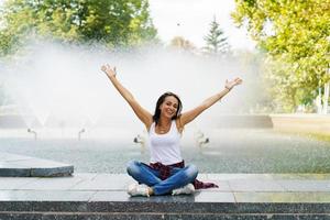 glad ung brunett kvinna mot bakgrund fontän Lycklig visar gest foto