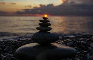 pyramid eller torn av sten stenar mot de bakgrund av de hav och de solnedgång himmel. zen stenar, meditation begrepp foto