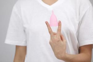 stänga upp av en ung kvinna händer innehav återanvändbar rosa silikon menstruations- kopp på vit t-shirt bakgrund. noll avfall menstruation hygien begrepp foto