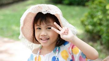 porträtt av Lycklig charmig 4 år gammal söt bebis asiatisk flicka, liten preschooler barn leende ser på kamera som visar 2 fingrar med kopia Plats. foto