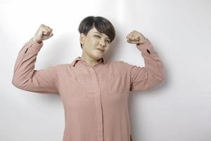 upphetsad korthårig asiatisk kvinna bär en rosa skjorta som visar stark gest förbi lyft henne vapen och muskler leende stolt foto