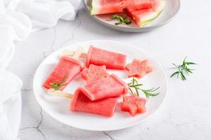 vattenmelon is grädde på en pinne och bitar av vattenmelon på en tallrik på de tabell. hemlagad efterrätt foto