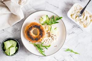 bagel smörgås med grädde ost, gurka och arugula på en tallrik. hemlagad frukost. topp se foto