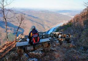 ung man med en ryggsäck från de tillbaka Sammanträde på en bänk och ser på de flod kanjon drina, serbia foto