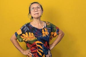 asiatisk äldre kvinna stående på henne midja på en gul bakgrund. foto
