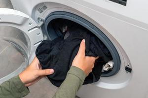 ung kvinna sätta tvätt i en tvättning maskin foto