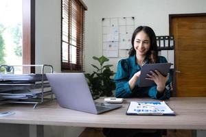 ung asiatisk affärskvinna arbetar på surfplatta med laptop på kontoret. foto