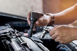 stänga upp gnista plugg spole i hand en man och använda sig av blockera rycka ta bort en bult i service i garage och motor rum bakgrund foto