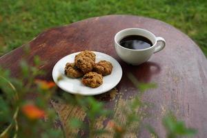 svart kaffe kopp med småkakor på trä- golv, svart kaffe i de morgon- till dryck med småkakor. foto