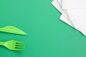 disponibel plast bestick grön. plast gaffel och kniv lögn på en grön bakgrund yta Nästa till bindor foto