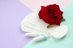 menstruations- dynor och tamponger med röd reste sig blomma på flerfärgad bakgrund foto