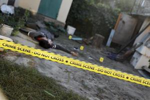 offer av en våldsam brottslighet i en bakgård av bosatt hus i kväll. död- man kropp under de gul polis linje tejp och bevis markörer på brottslighet scen foto