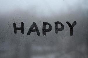 de engelsk ord Lycklig är skriven med en finger på de yta av de dimma glas foto