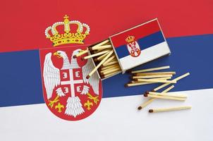 serbia flagga är visad på ett öppen tändsticksask, från som flera tändstickor falla och lögner på en stor flagga foto