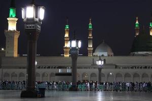 skön natt se av masjid al nabawi, medinas grön kupol, minareter och moské gård. foto