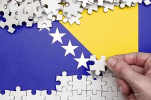 bosnien och herzegovina flagga är avbildad på en tabell på som de mänsklig hand veck en pussel av vit Färg foto
