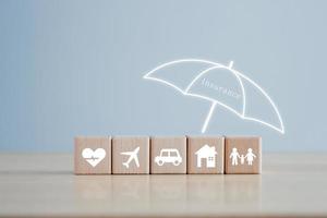 försäkring begrepp. skydd mot en möjlig eventualitet. paraply omslag hus, bil, familj, resa och hälsa ikon på trä- blockera för försäkran liv begrepp. foto